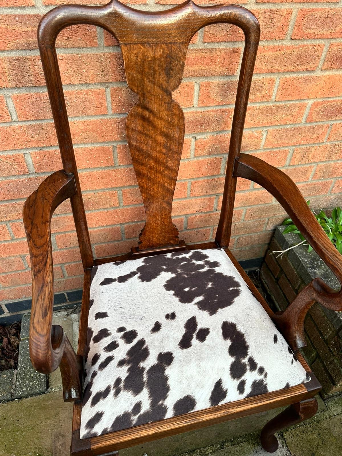 Wooden chair with cowhide upholstery and carved backrest against a brick wall.