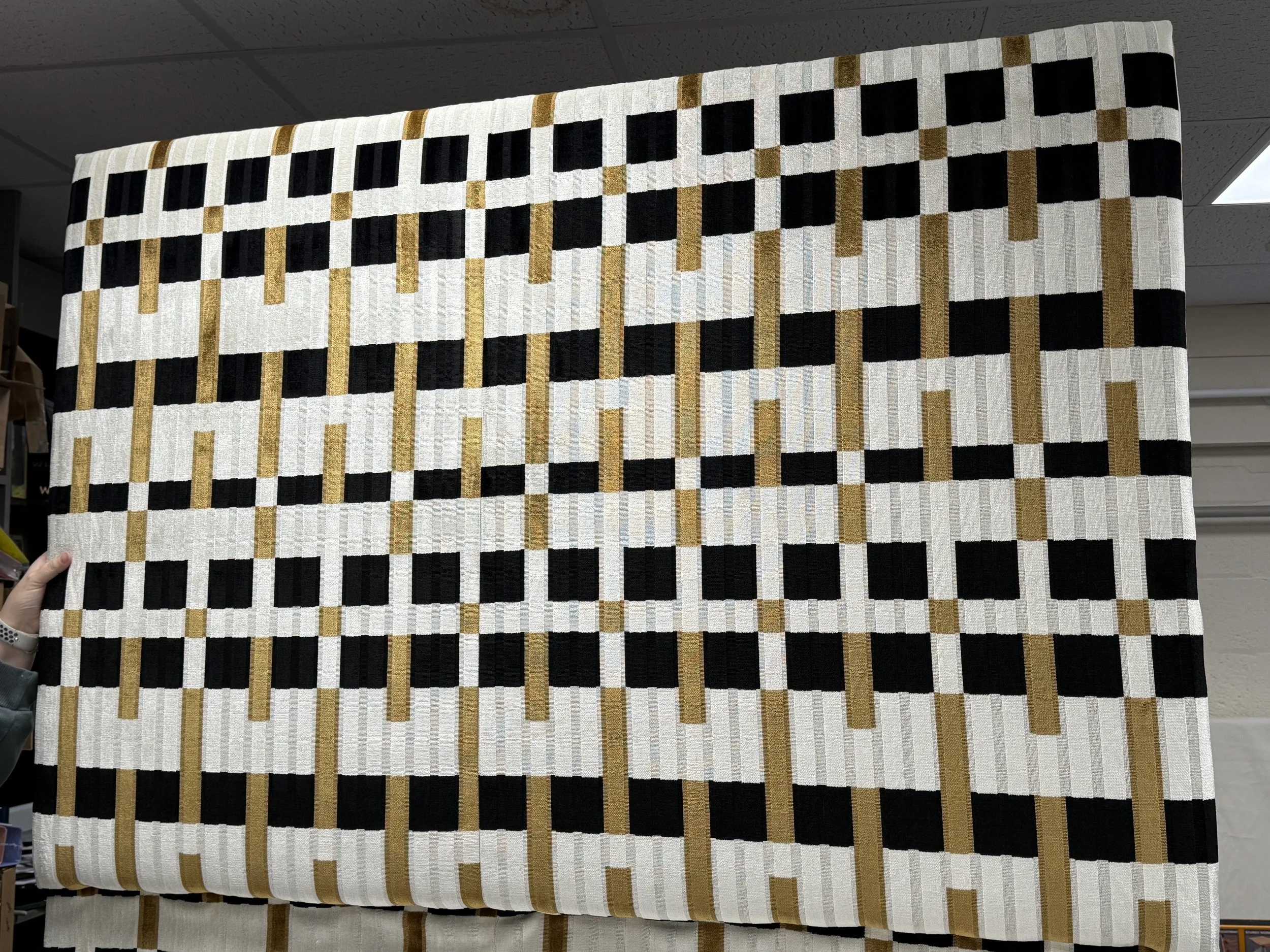 A geometric patterned rug with black, white, and tan designs held up in a store.