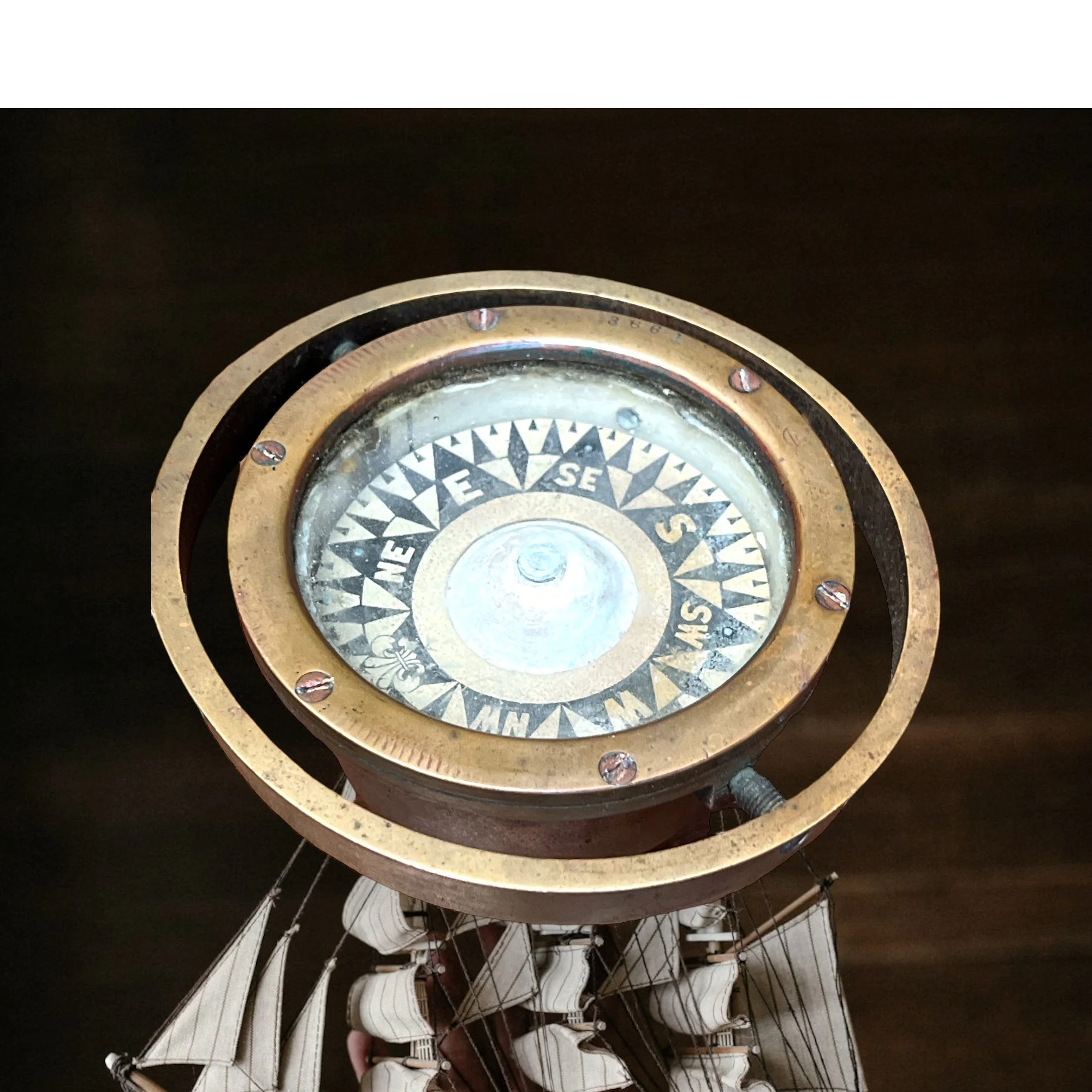 Antique brass compass with cardinal directions, positioned on a model ship's deck.