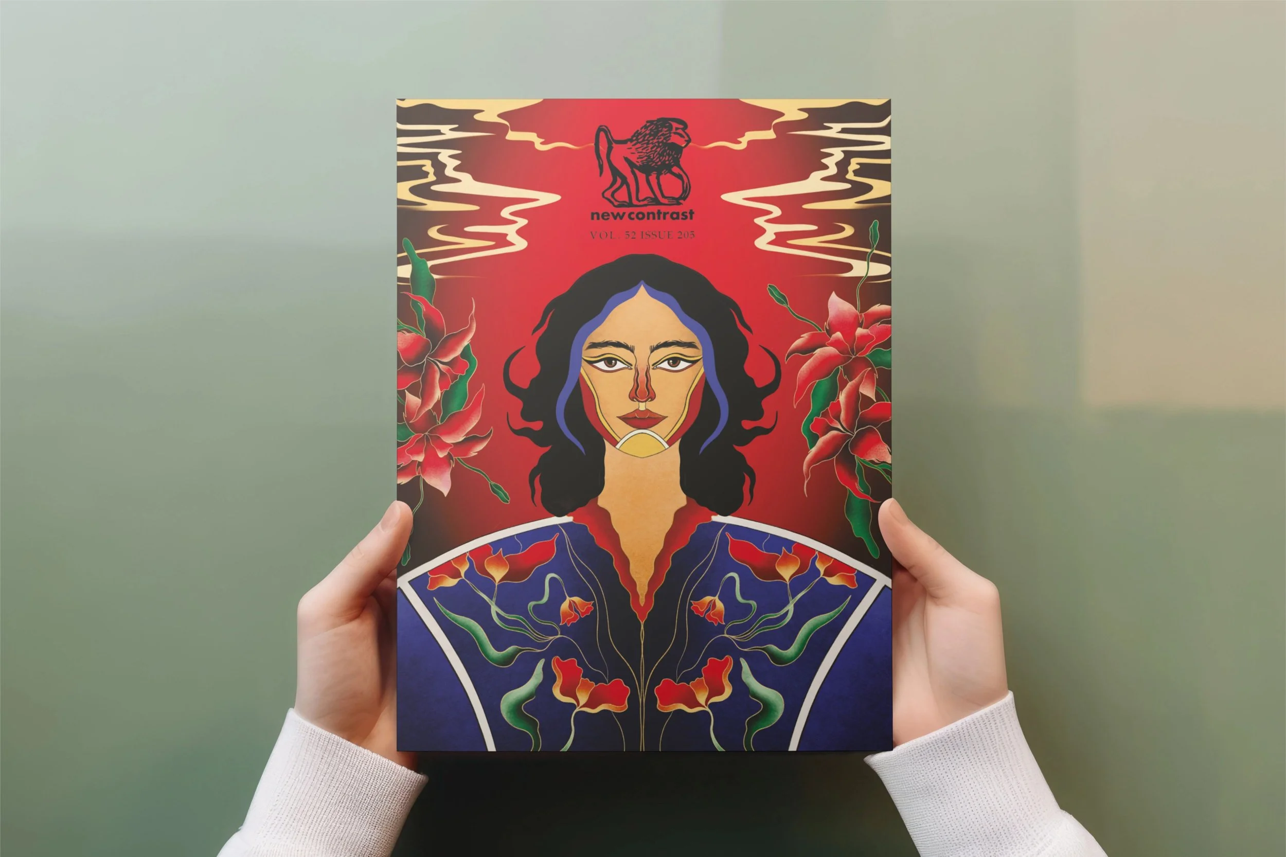 A person is holding a colorful illustrated magazine cover featuring a woman's face with long black hair, surrounded by red flowers and green vines, with a red background and a black lion logo at the top.