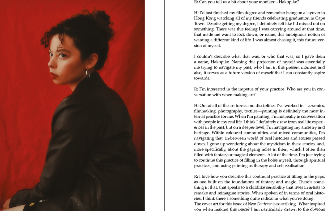 A woman with short curly black hair, silver hoop earrings, and a dark leather jacket poses against a red background.