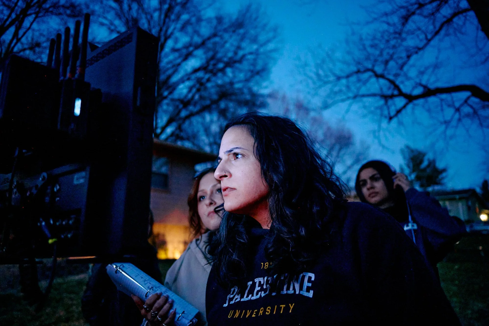 Women on a film set outdoors during dusk, with equipment and trees visible in the background.