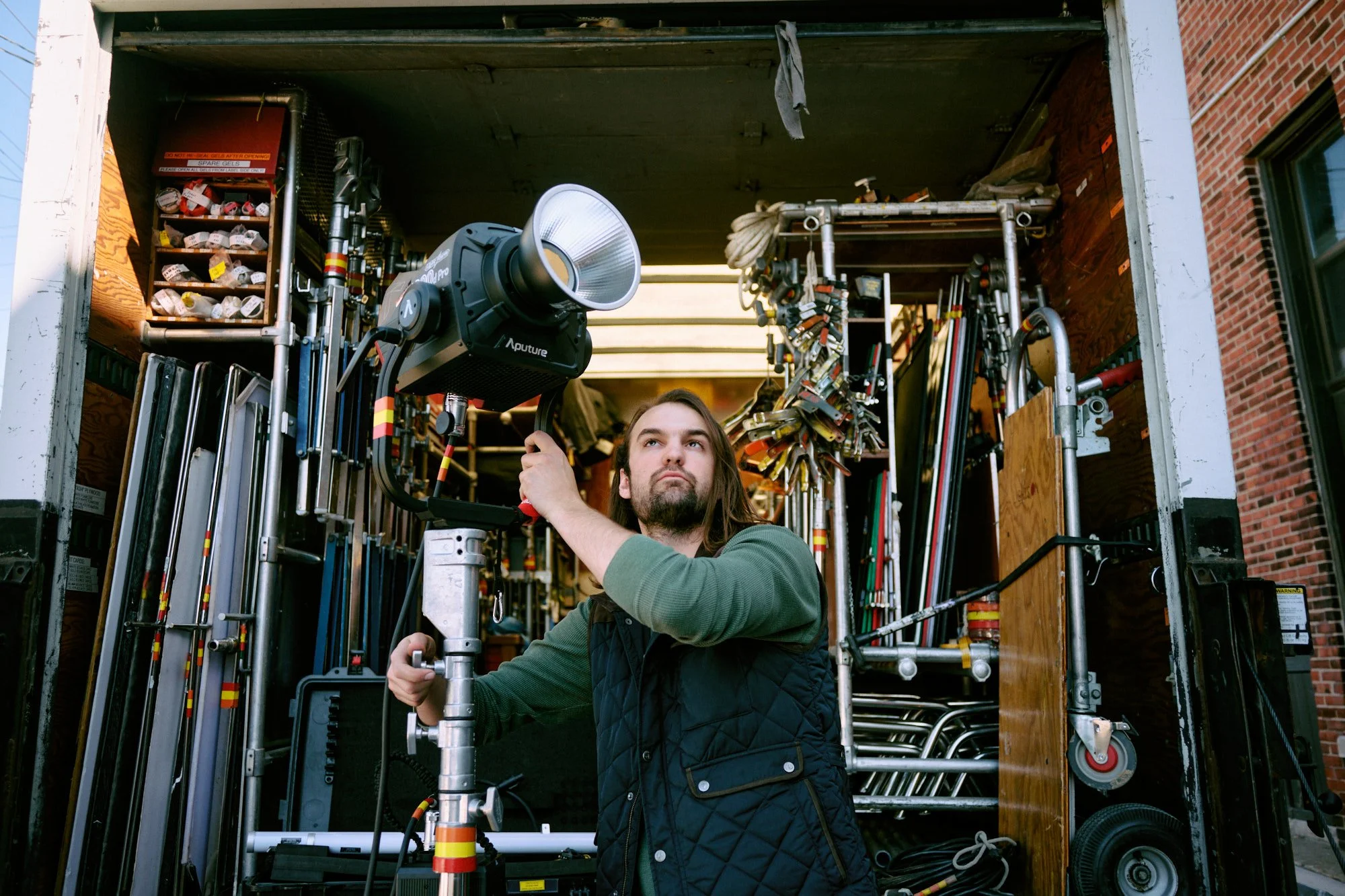 A man operating film or photography equipment inside a truck with various machinery and tools around him.