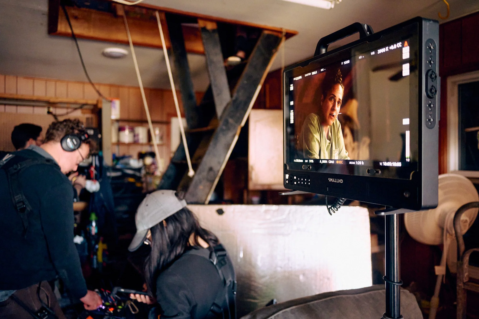 Filmmaking crew on set with monitor showing actress's close-up shot, in cozy wooden interior