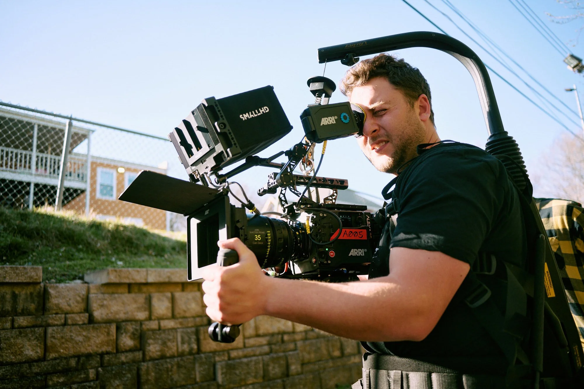 A man operating a professional video camera outdoors on a sunny day.
