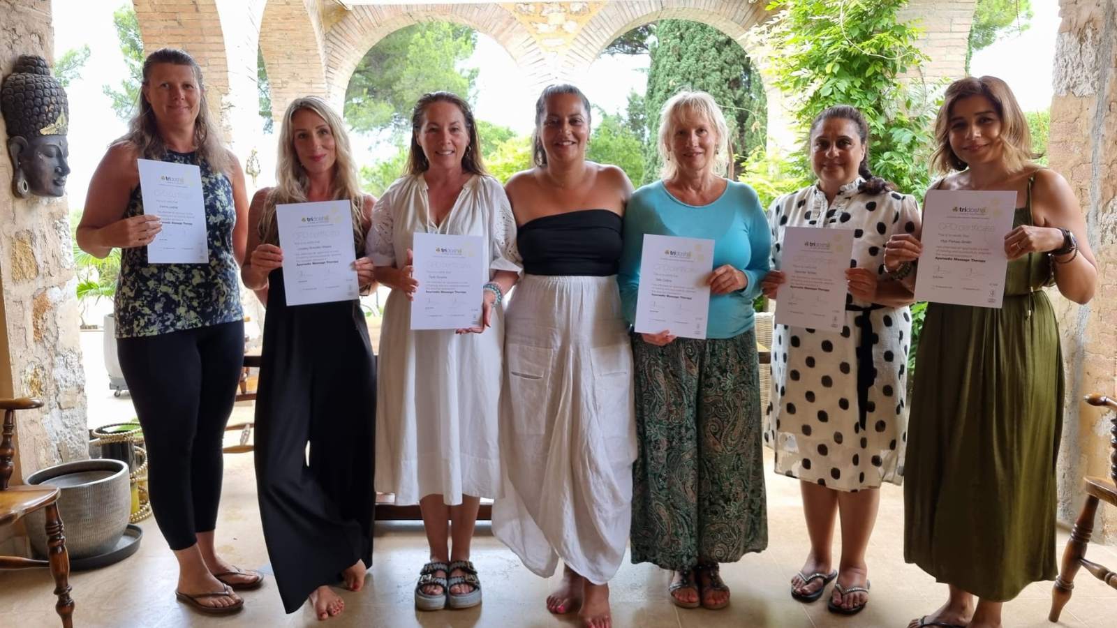 Seven women stood in front of archways holding certificates