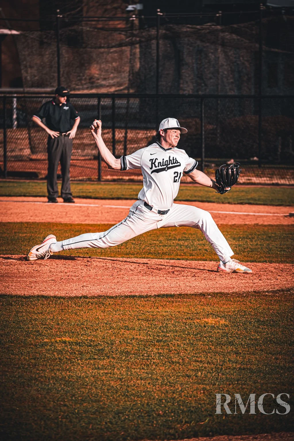 A baseball player in a uniform with 'Knights' on it, caught mid-throw on the field, with an umpire in the background.