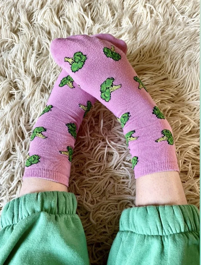 Emma's feet wearing colourful, fun, pale pink socks with bright green broccoli patterns on.