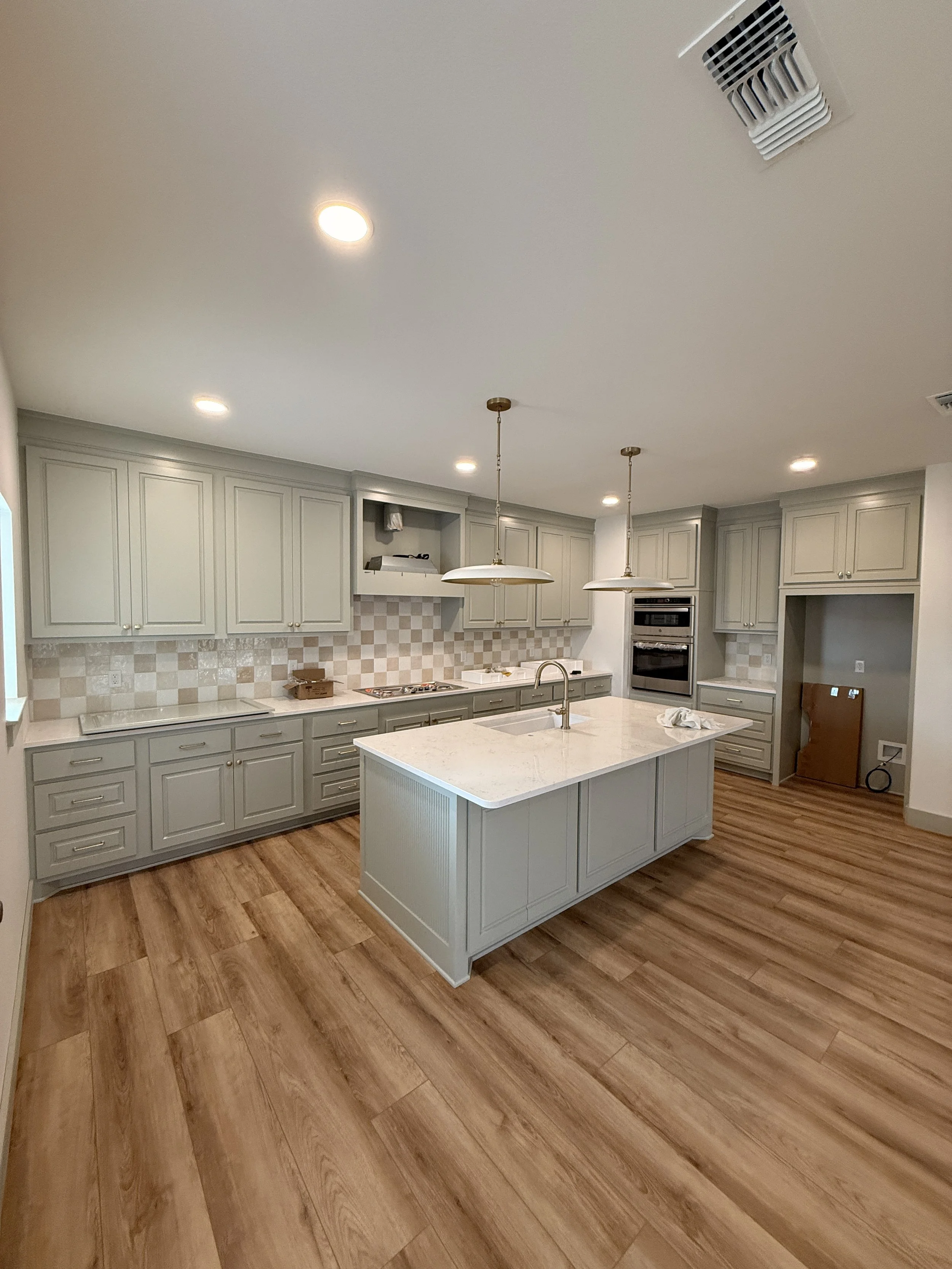 Modern kitchen with light gray cabinets, a white island with a sink, pendant lighting, and wood flooring.