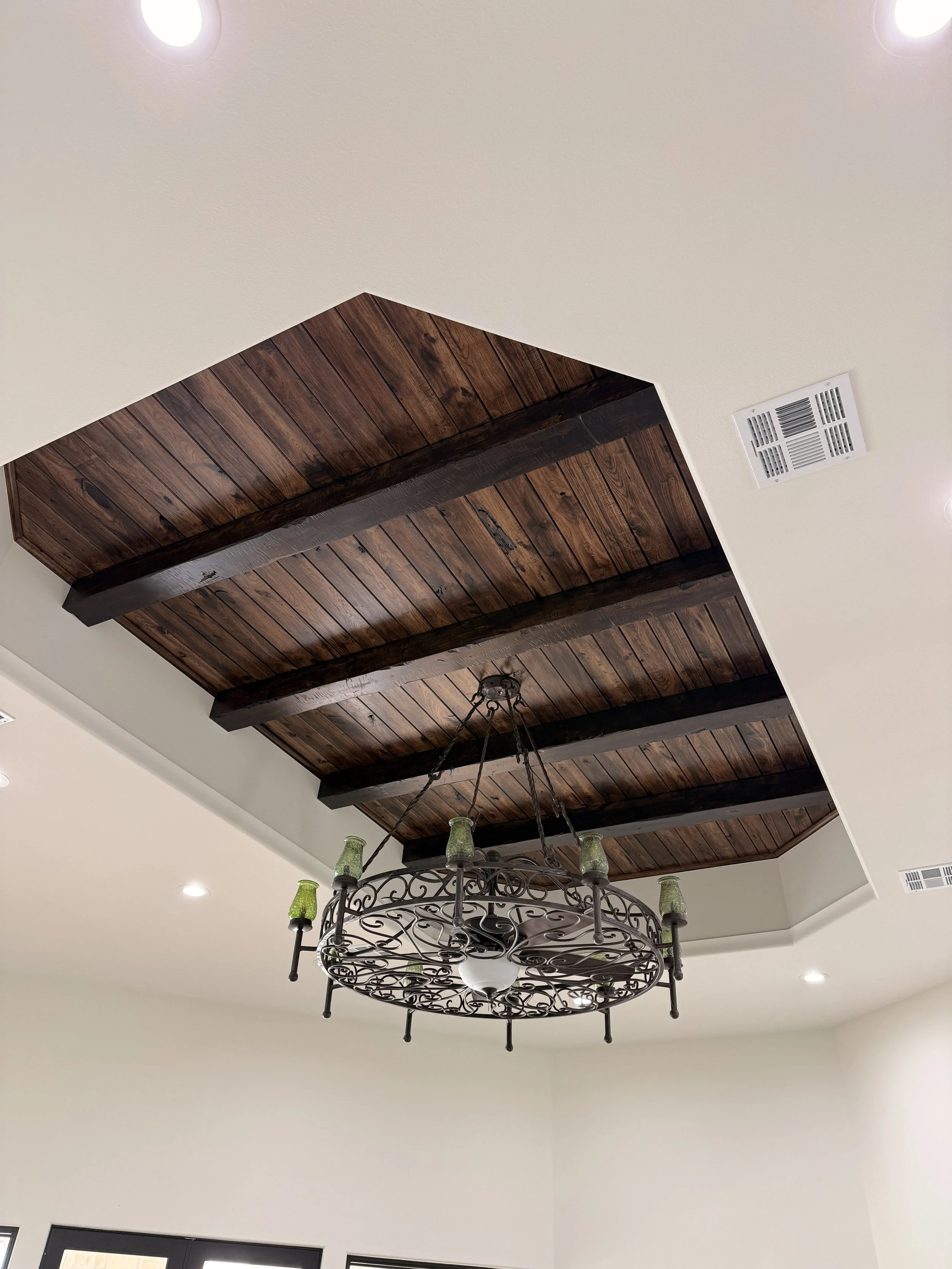Ceiling with wooden panels, black beams, and a decorative wrought-iron chandelier with green glass shades.