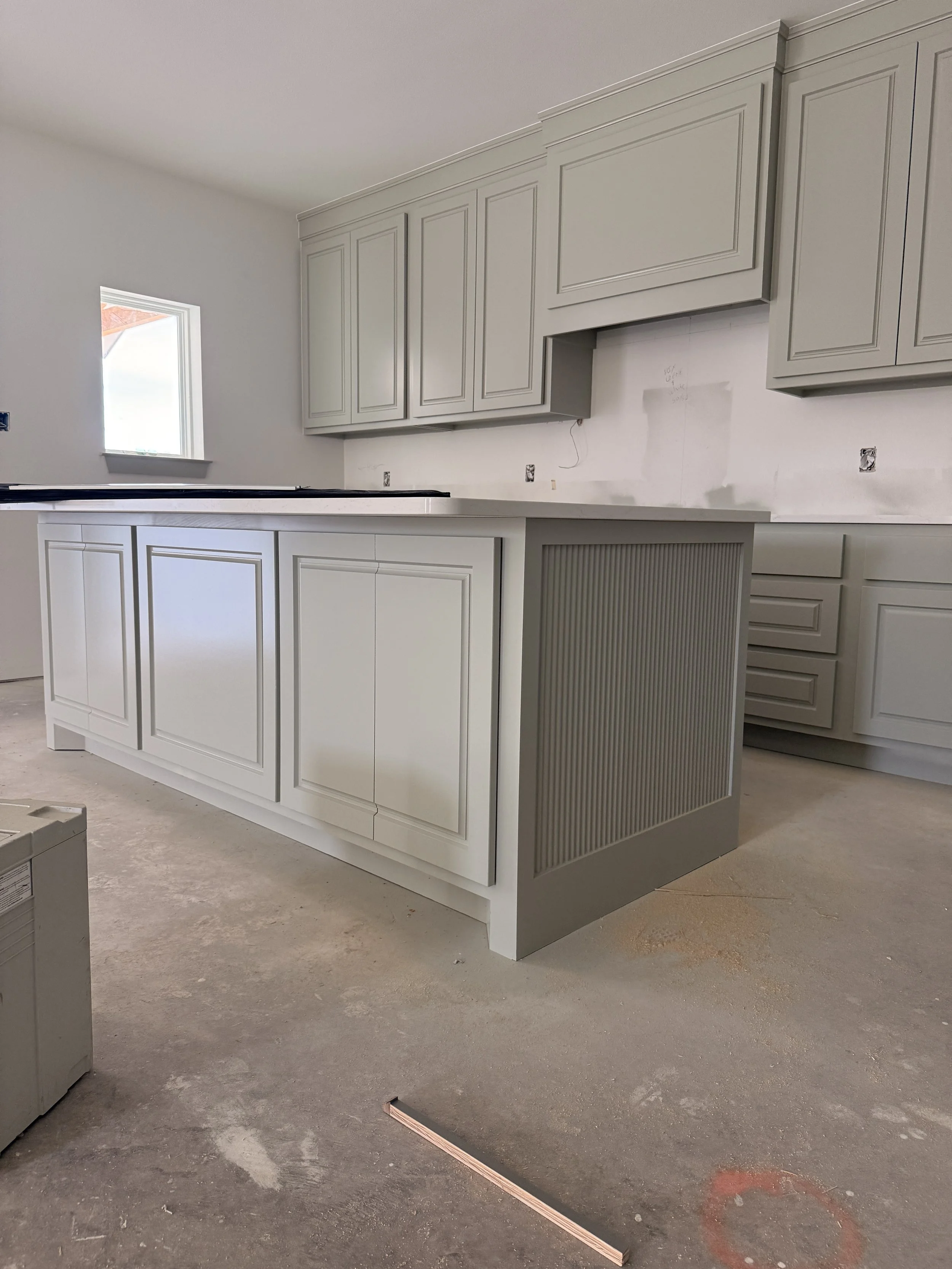 Unfinished kitchen with white cabinets and island, construction materials on concrete floor.