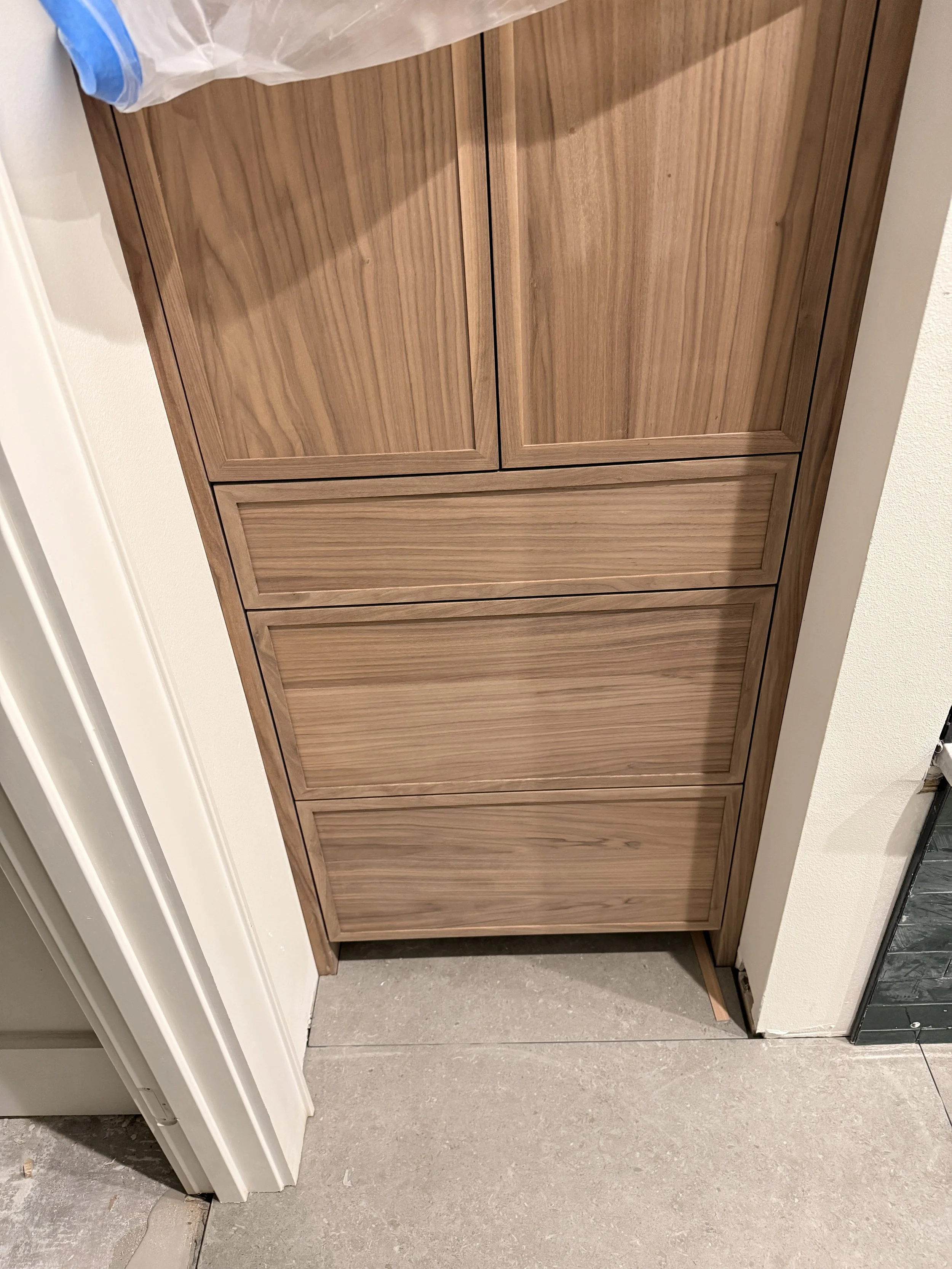 A wooden cabinet with four drawers, situated on a concrete floor next to a wall and a partially visible door frame.