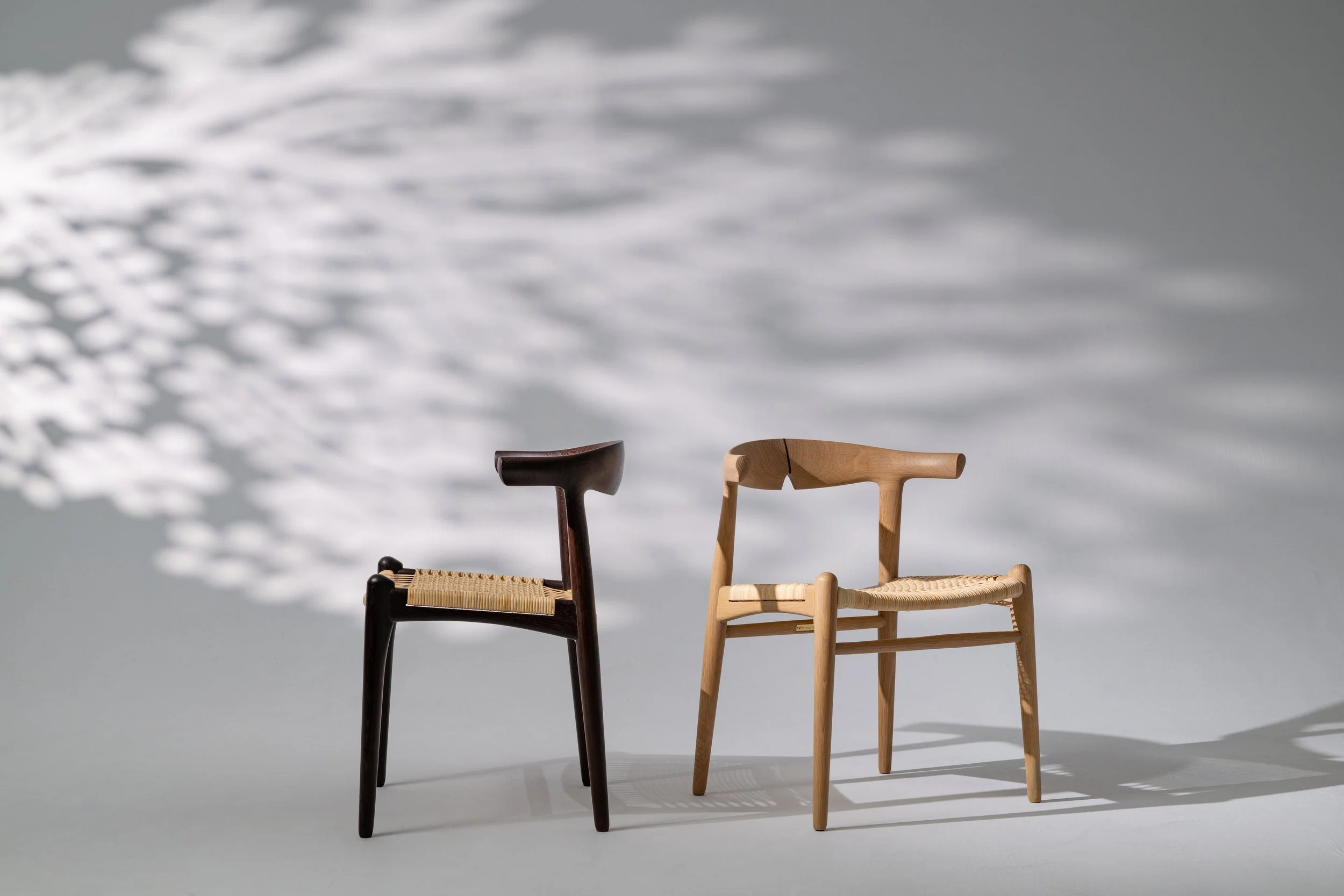 Two handmade wooden chairs with woven seats in dappled light