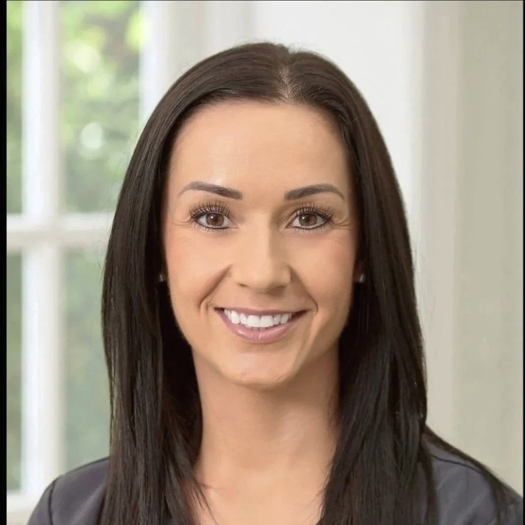 Black and white headshot of a woman with long, straight hair, smiling, in front of an abstract background.