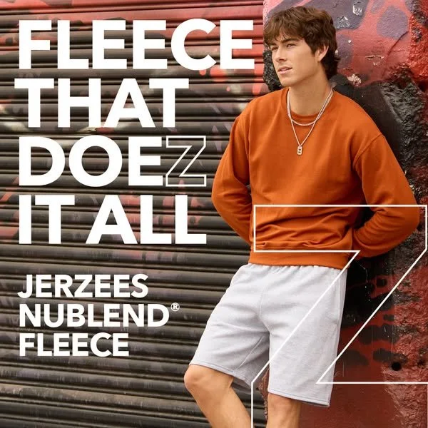 A young man leans against a wall with graffiti, wearing an orange sweatshirt and white shorts, with text promoting Jerzees Nublend fleece clothing.
