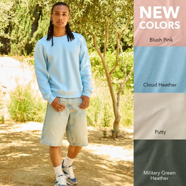 A young woman in a light blue sweatshirt and denim shorts standing outdoors with trees in the background. On the right side, a color swatch panel shows new sweatshirt colors: blush pink, cloud heather, putty, and military green heather.