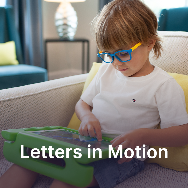 A first grade reader wearing glasses sitting on a couch and using a tablet device.