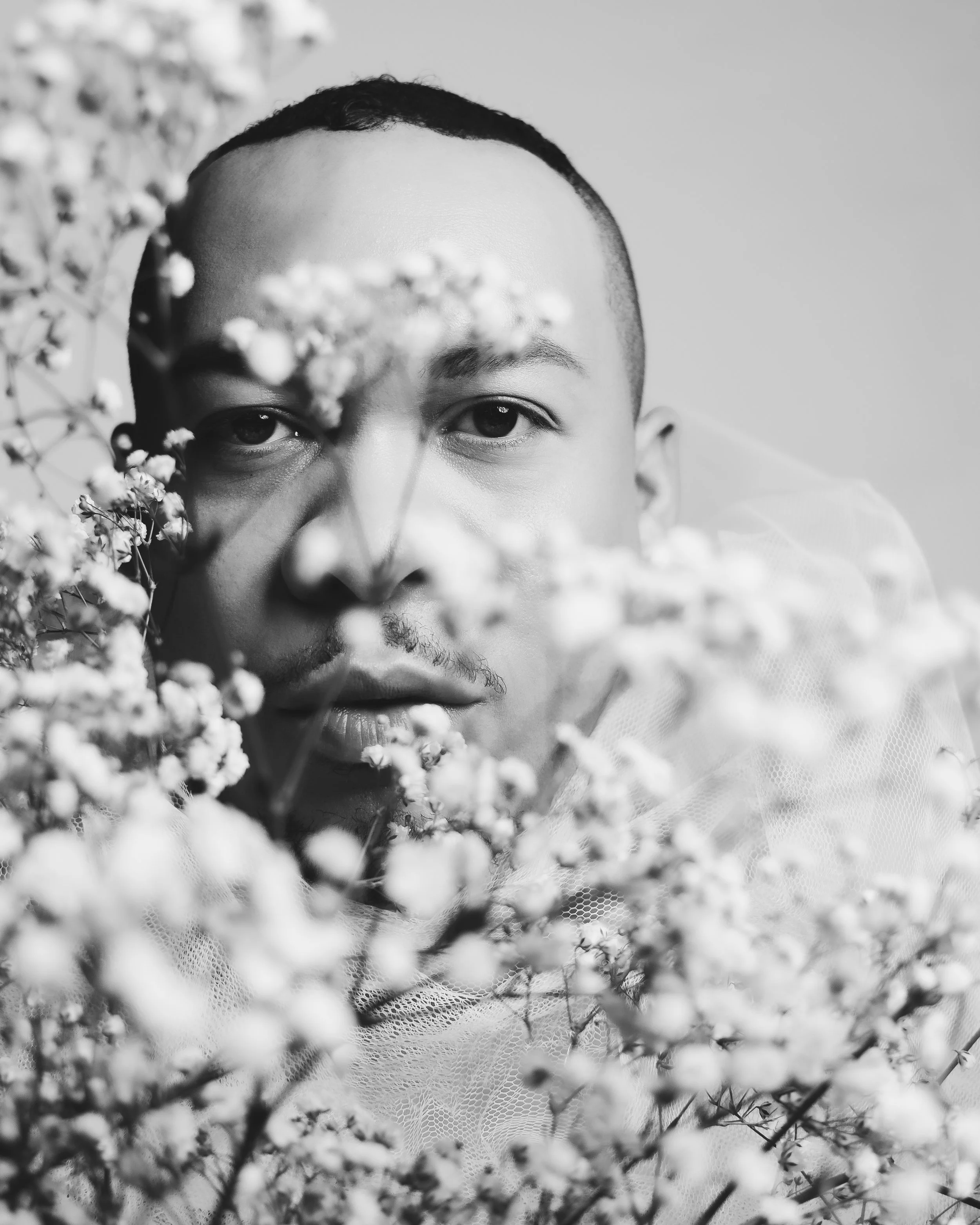 Black and white portrait of a person peeking through baby's breath flowers.