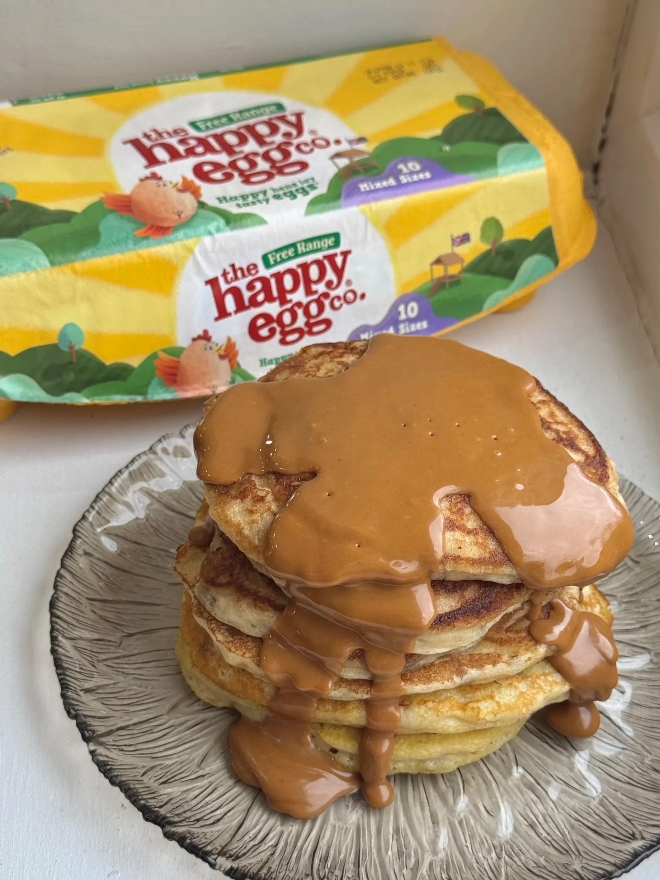 Stack of pancakes topped with caramel syrup on a glass plate in front of a box of Happy Egg Co. eggs - UGC content creation.