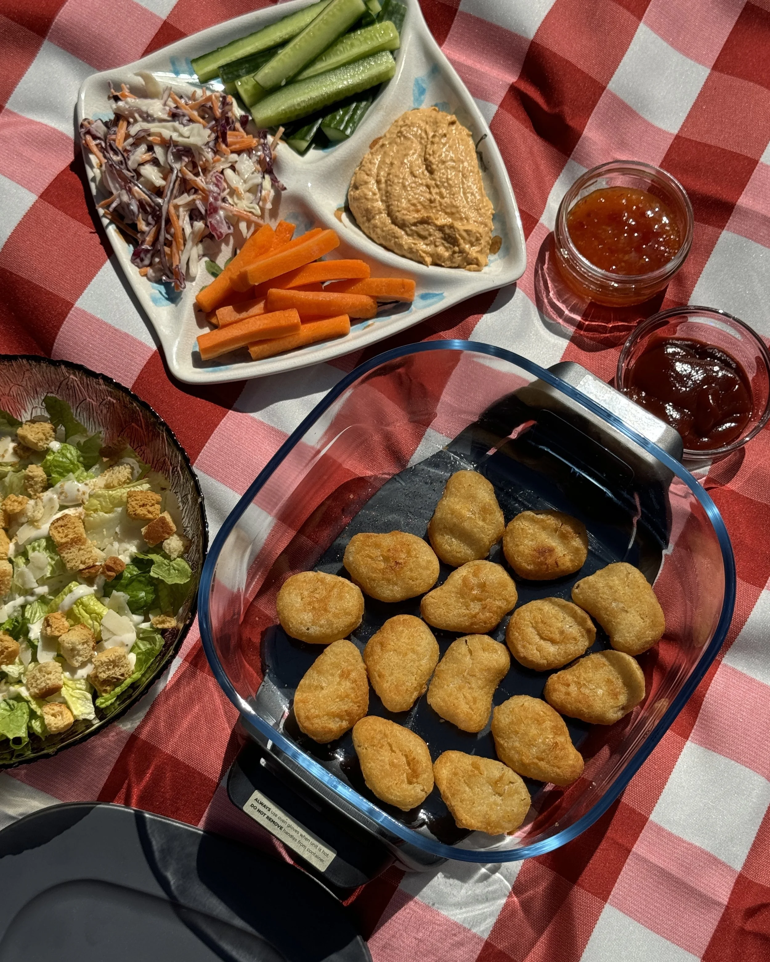 Plate of fried chicken nuggets, a salad with croutons, a vegetable tray with celery, carrots, coleslaw, hummus, and two small bowls of dipping sauces - Quorn Foods UGC content creation picnic