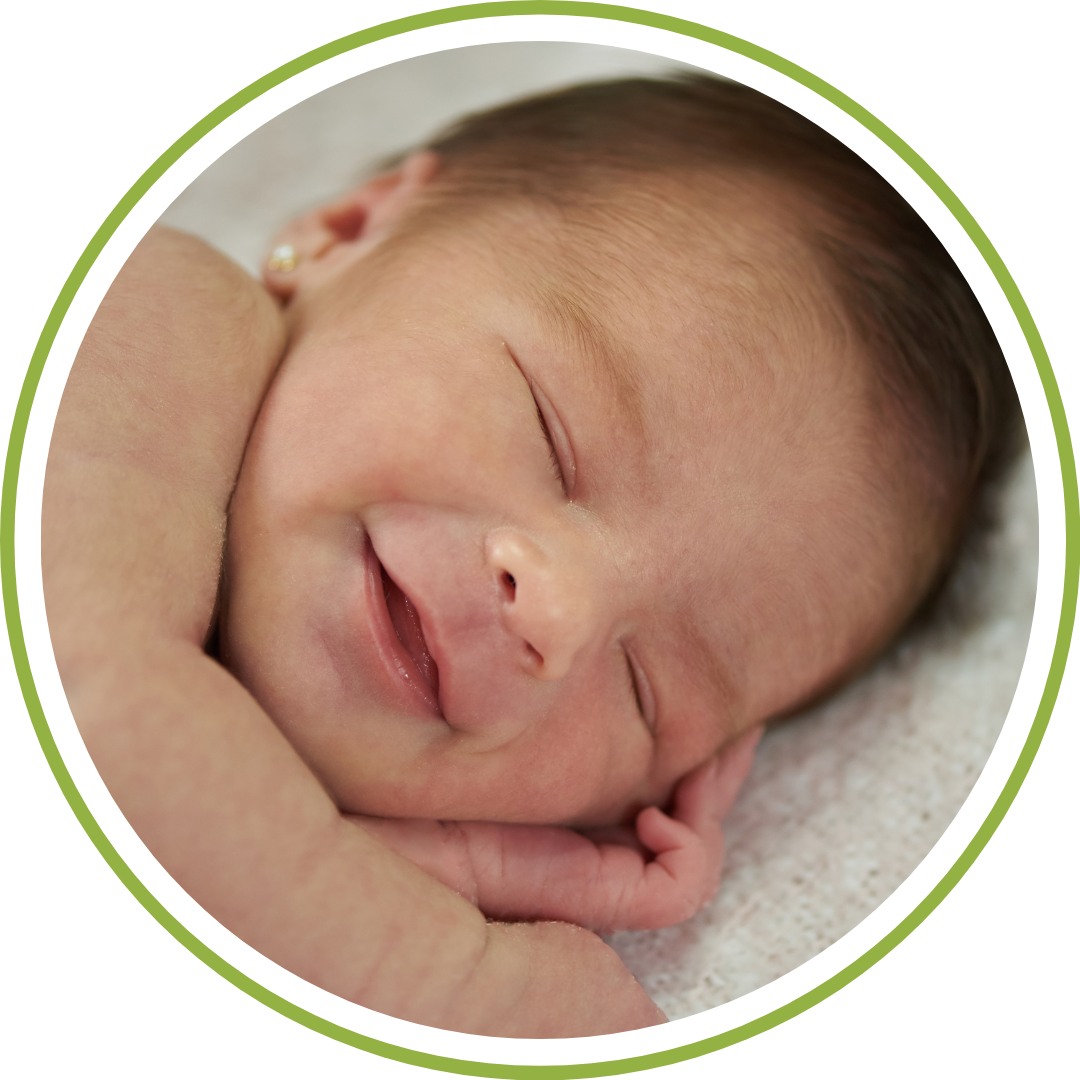 newborn baby sleeping in a wooden bassinet, wearing a soft cotton swaddle with their eyes tightly closed and a slight, tiny smile on their face.