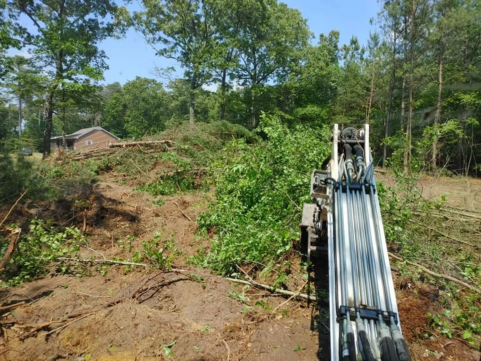 Excavator clearing trees and debris from a wooded area during land clearing project.