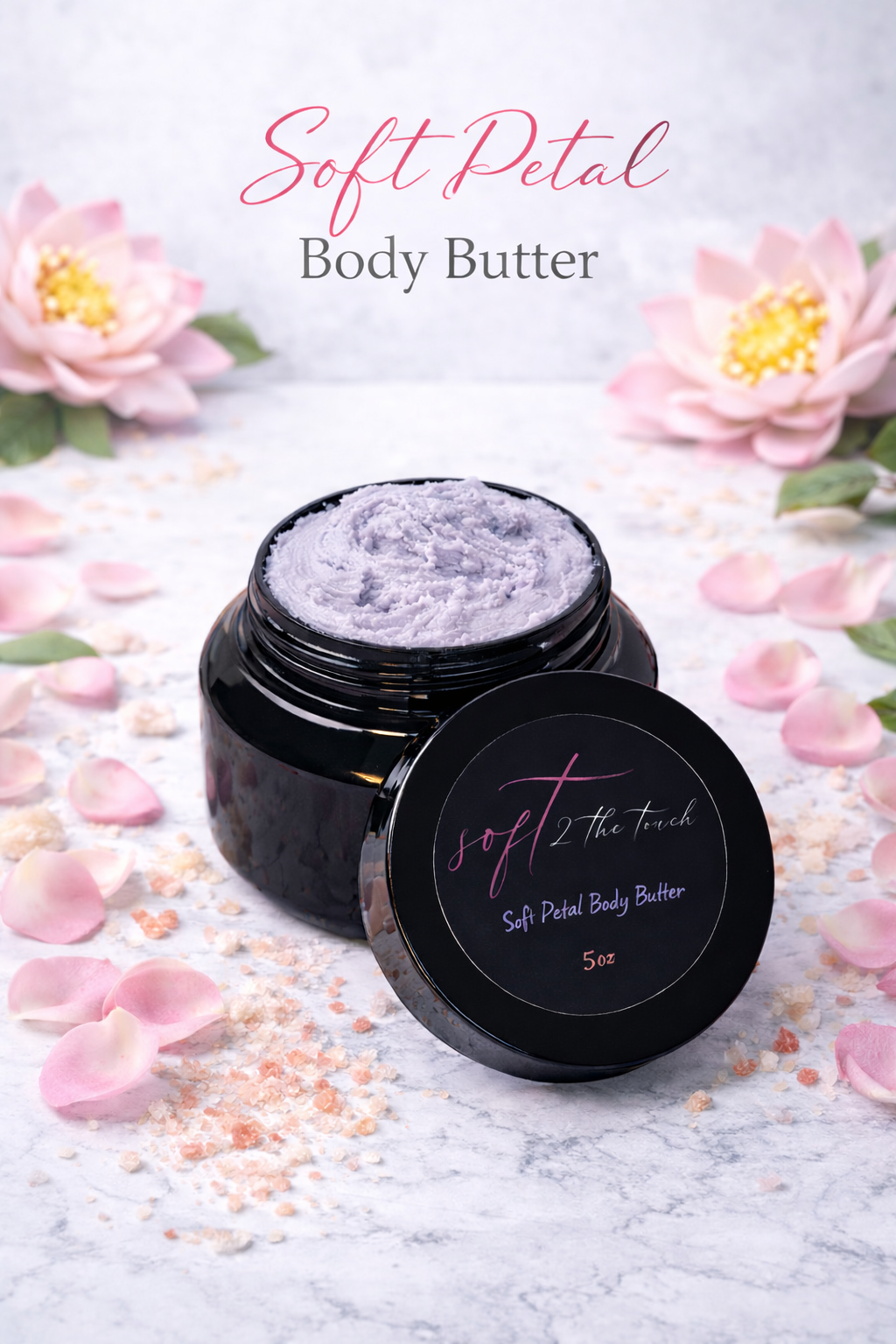 A jar of soft petal body butter surrounded by pink flowers and scattered pink petal and salt flakes on a white textured surface.