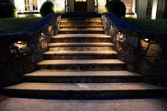 Stone steps with small lights along the sides leading up to a house entrance at night.