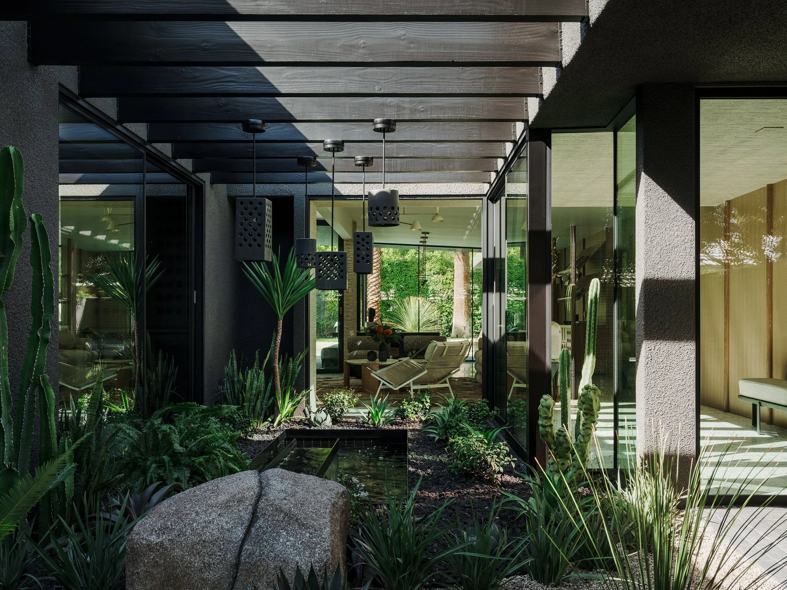 Modern house with outdoor patio, large glass sliding doors, plant life including cacti, and overhead black pendant lights.