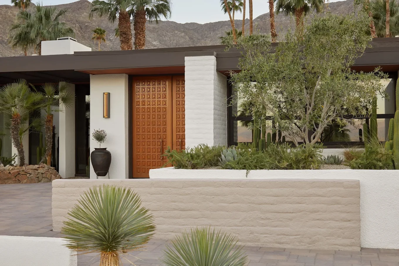Modern house exterior with desert landscaping, tall palm trees, and mountain backdrop.