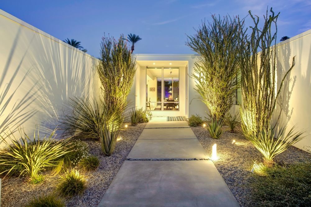 Modern house entrance with concrete pathway, desert plants, and outdoor lighting in the evening.