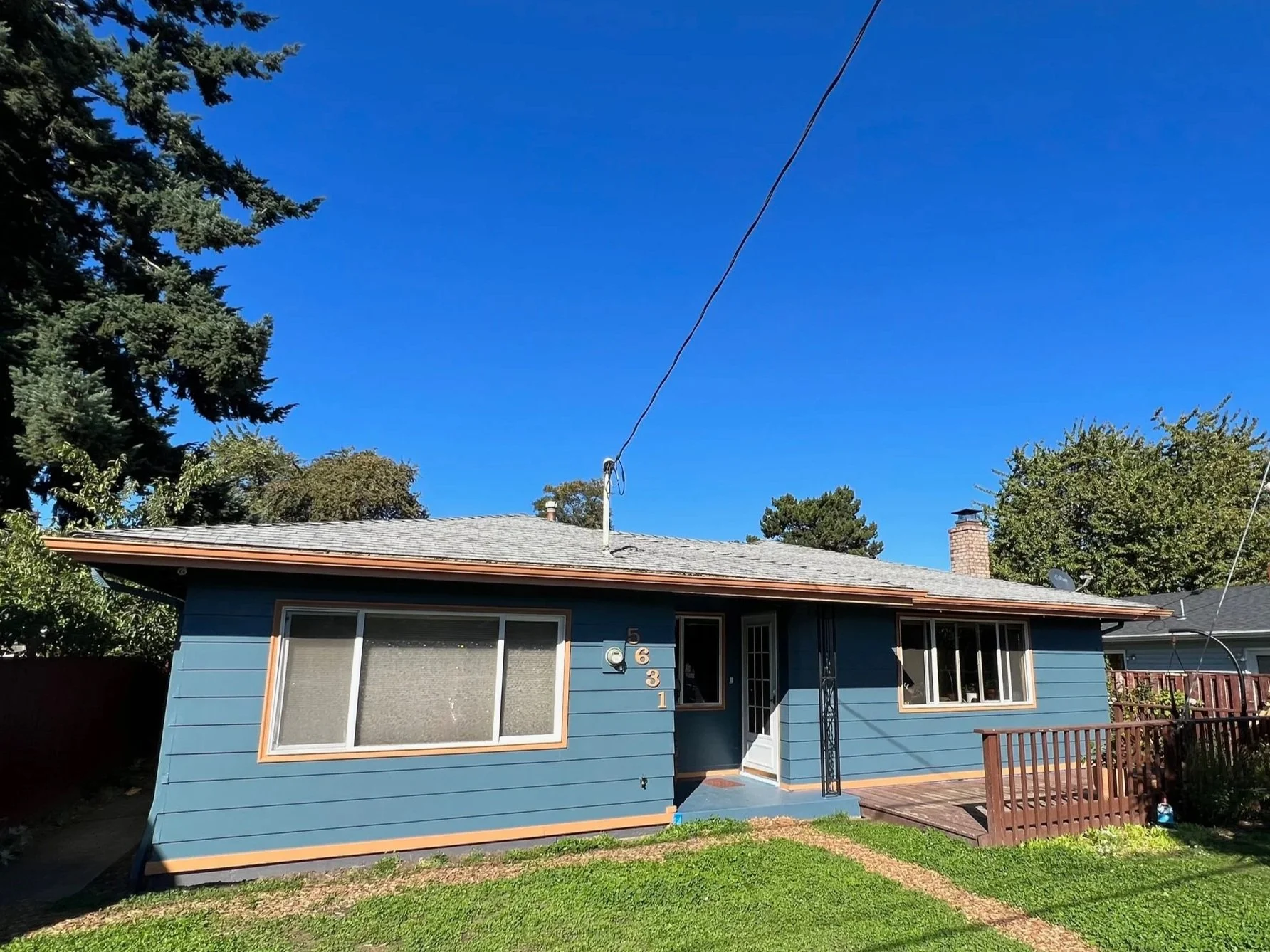 Front view of a blue house with a small porch, green lawn, trees, and a clear blue sky.