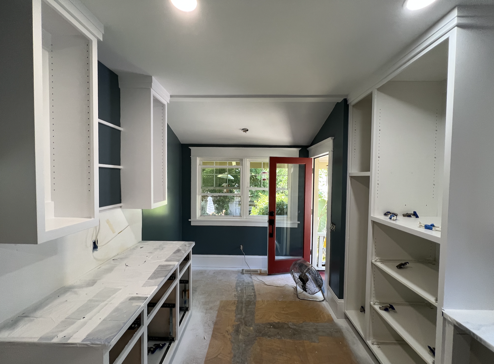 Interior view of a small room with white cabinets on the left, a window on the right, and fish-themed wallpaper on the wall in the background.