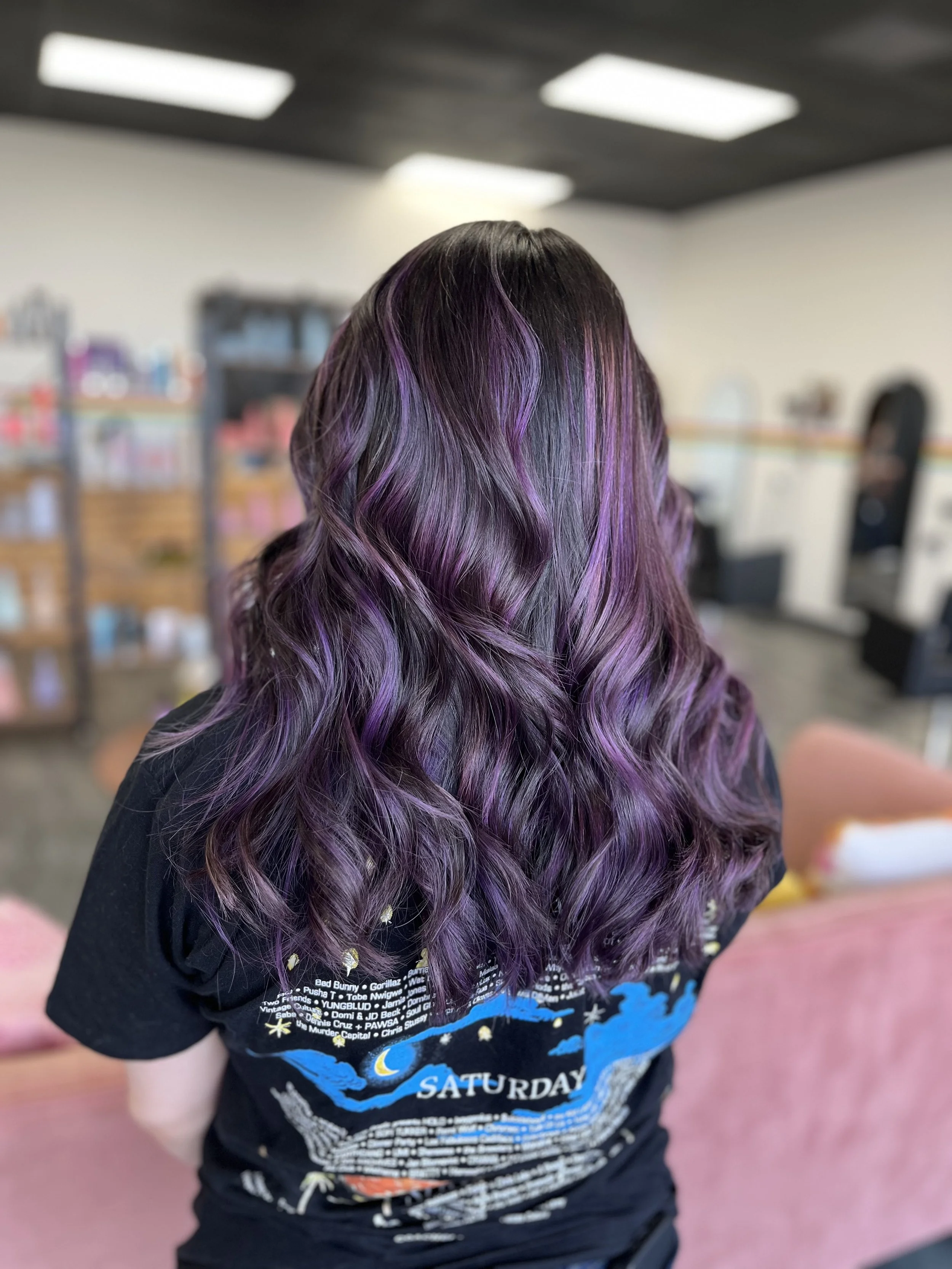 Person with long wavy hair featuring black and purple highlights, turned away from the camera indoors.