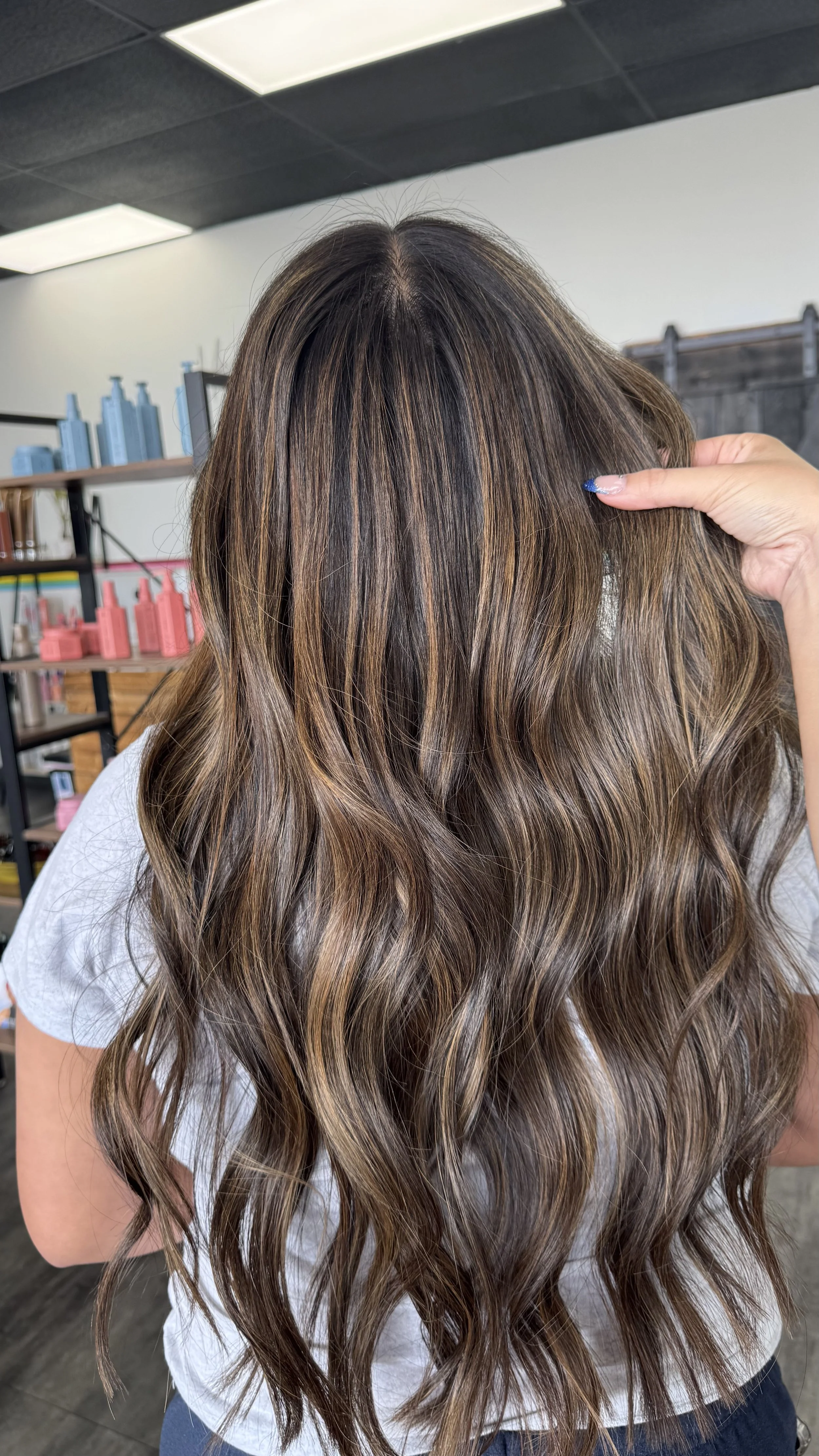 Woman with long, wavy hair that has caramel highlights and darker roots, in a salon.