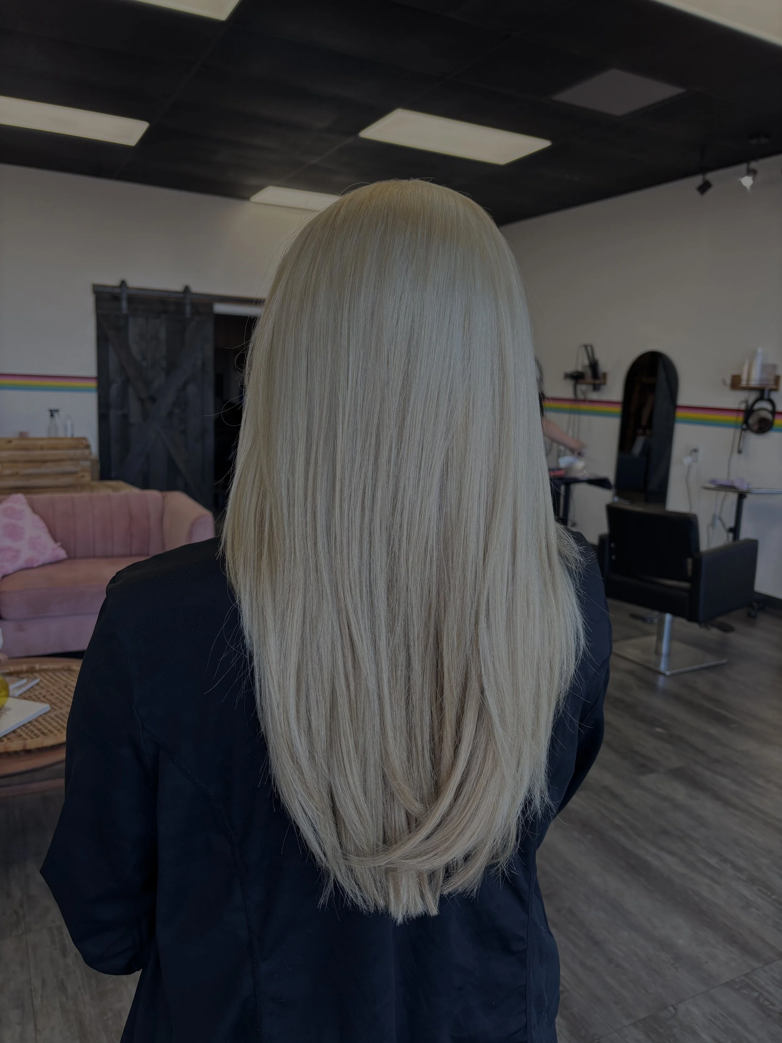 Back of a woman with long, straight, platinum blonde hair in a salon.