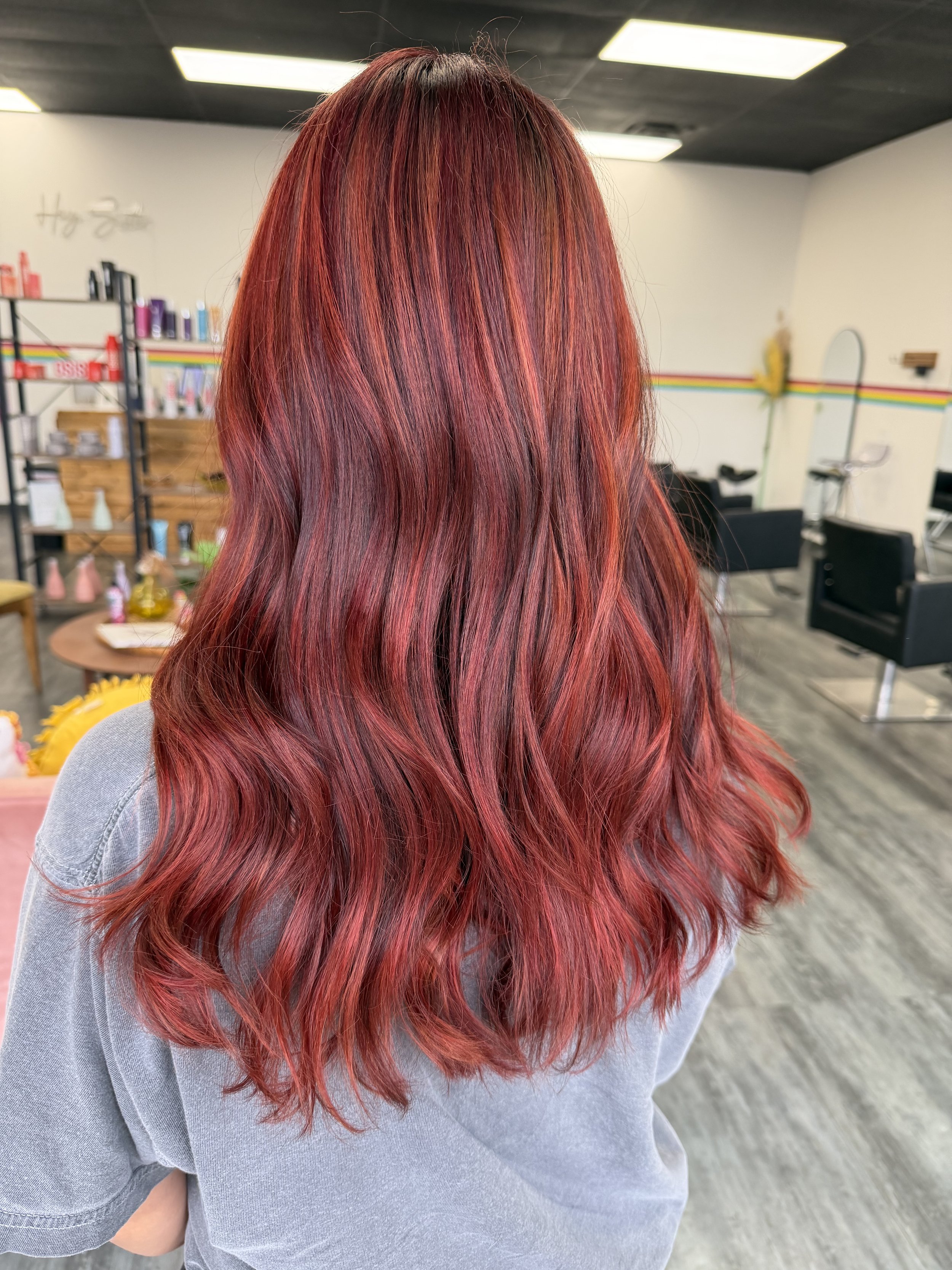 Back view of a woman with long, red, wavy hair in a salon or hair studio.