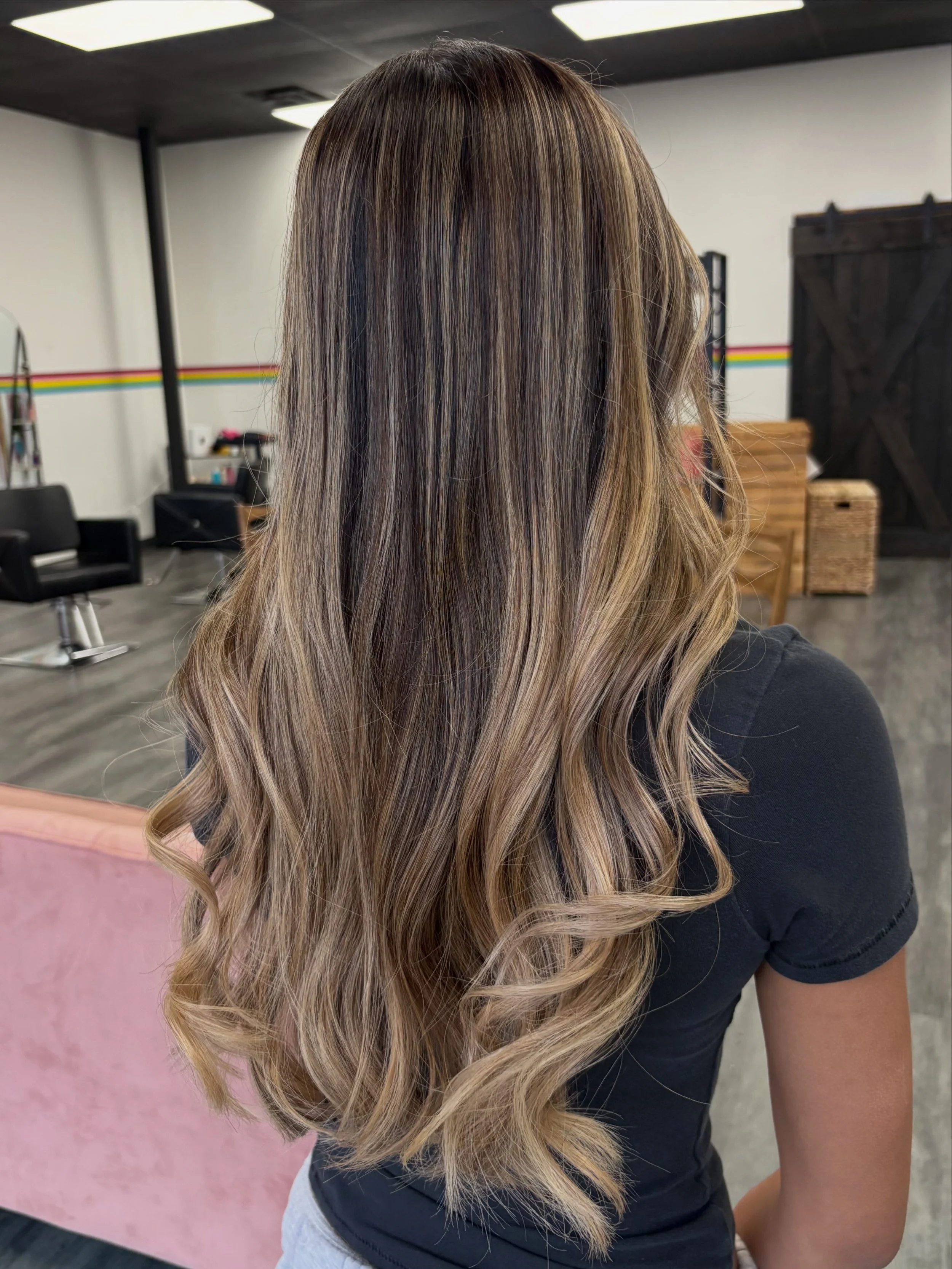 Woman with long, wavy, highlighted hair in a salon setting.