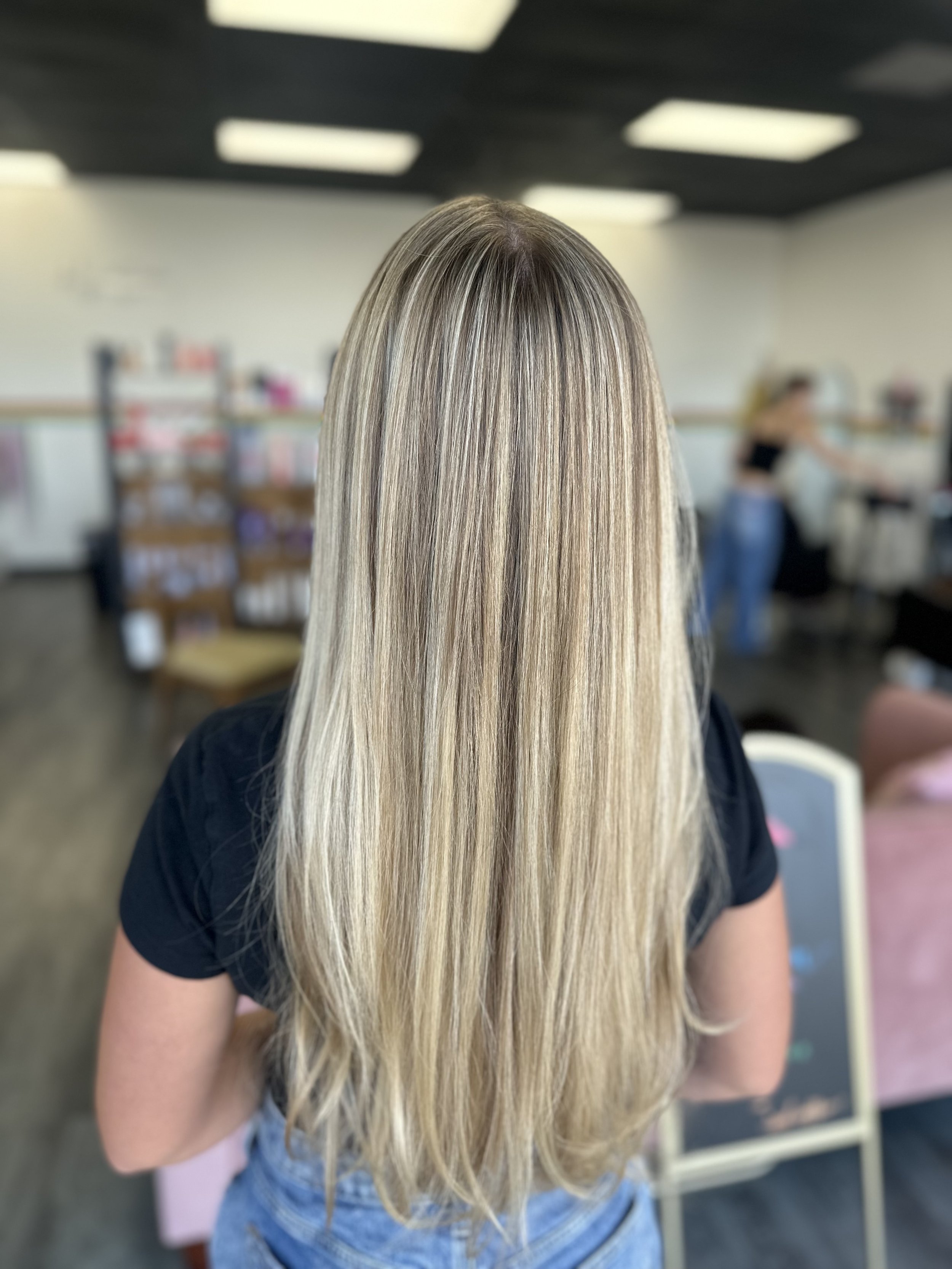 Back view of a woman with long, straight, blonde hair in a salon or studio setting.