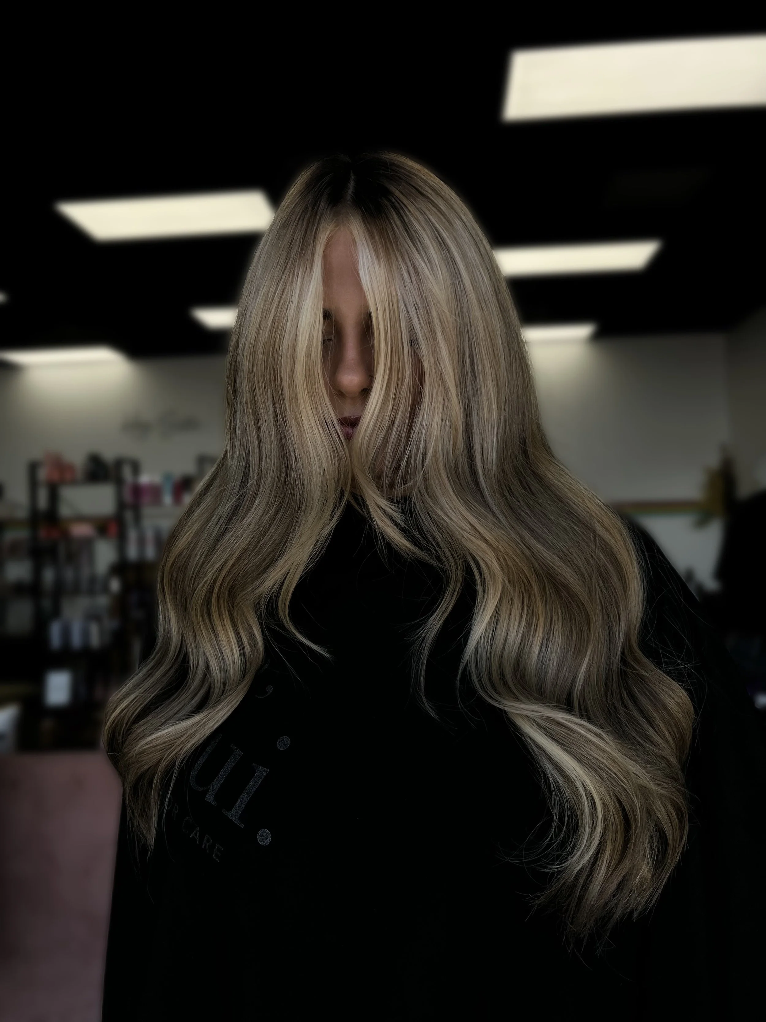 Person with long, wavy blonde hair in a salon or studio setting