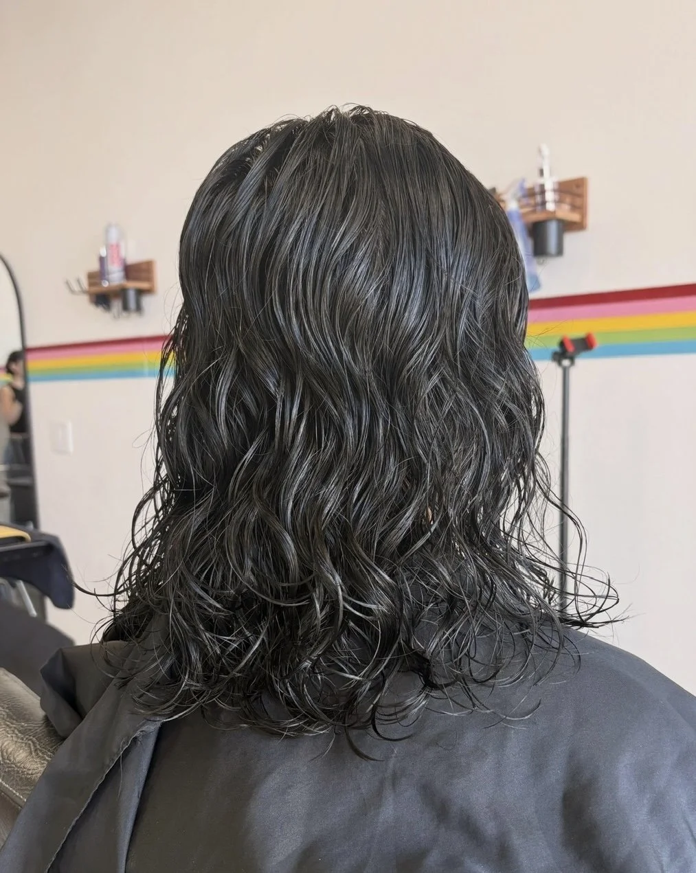Back of a person with wet dark, curly hair in a salon setting.