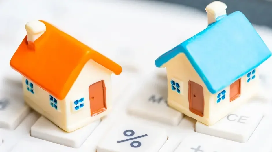 Two small ceramic houses with colorful roofs, one orange and one blue, placed on financial calculator keys.