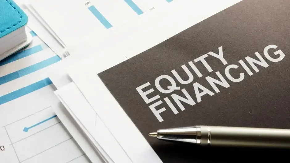 A pen resting on a black booklet titled 'Equity Financing', with several sheets of paper with blue bar graphs and a notebook partially visible in the background.