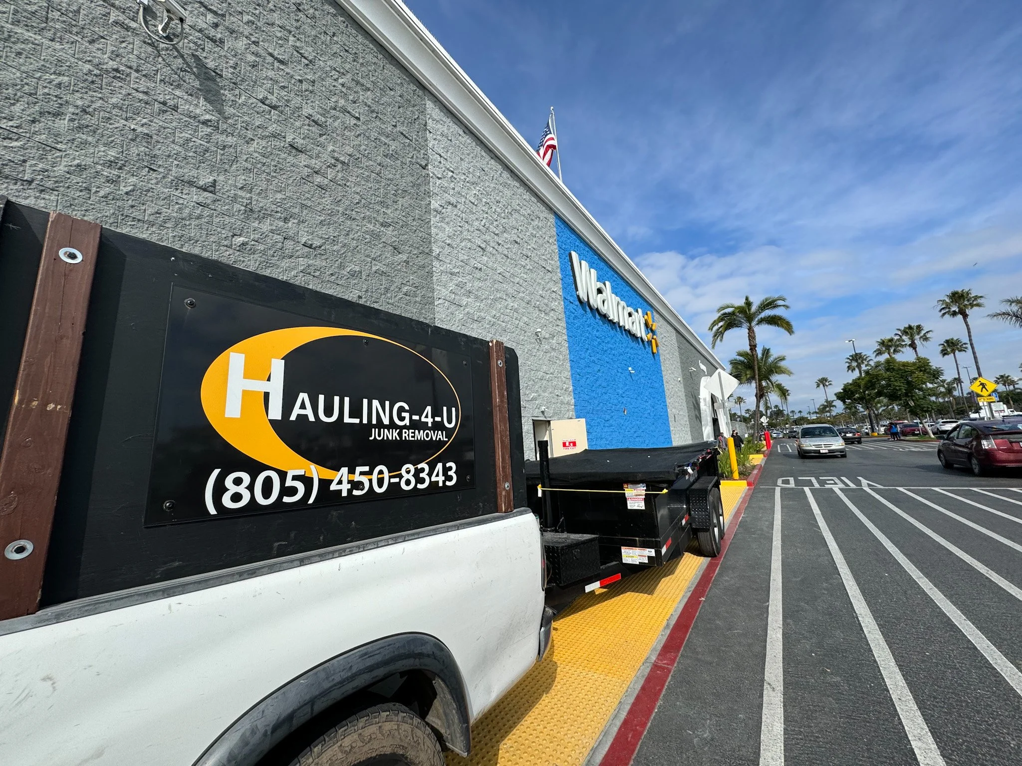 Walmart storefront with parking lot, Palms trees, and a junk removal truck in the foreground.