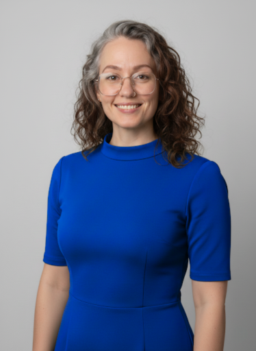 A woman with curly brown hair, wearing glasses and a bright blue dress, smiling at the camera against a plain gray background.