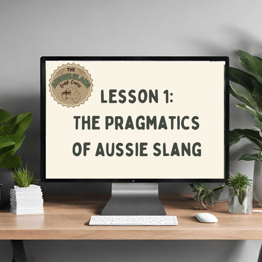 Computer monitor displaying "Lesson 1: The Pragmatics of Aussie Slang" with a logo titled "The Aussie Slang Crash Course." The setup includes a keyboard, mouse, potted plants, and a stack of papers on a wooden desk.