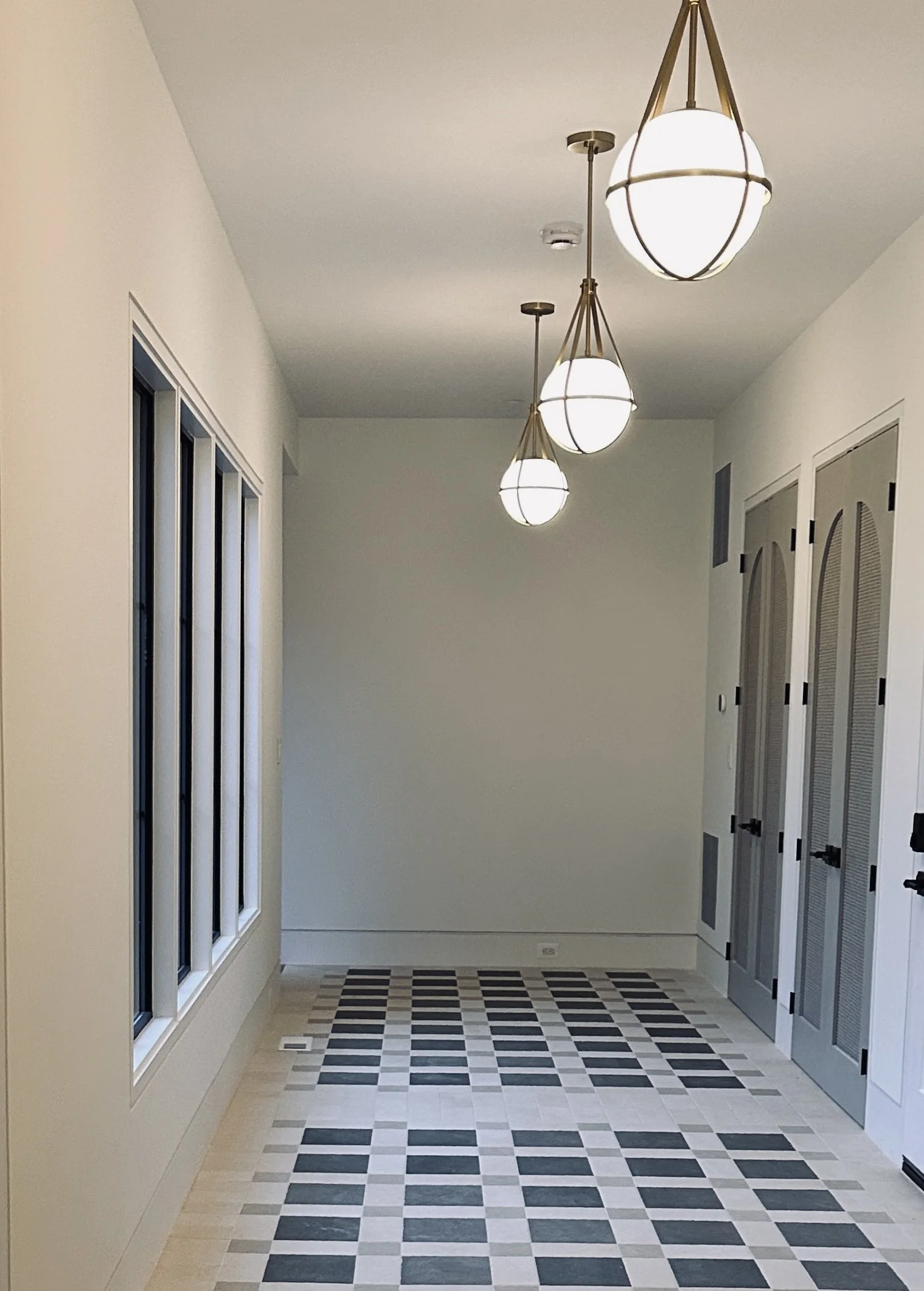 Elegant curved brass light fixtures hanging in a minimalist mudroom hallway with arched doorways.