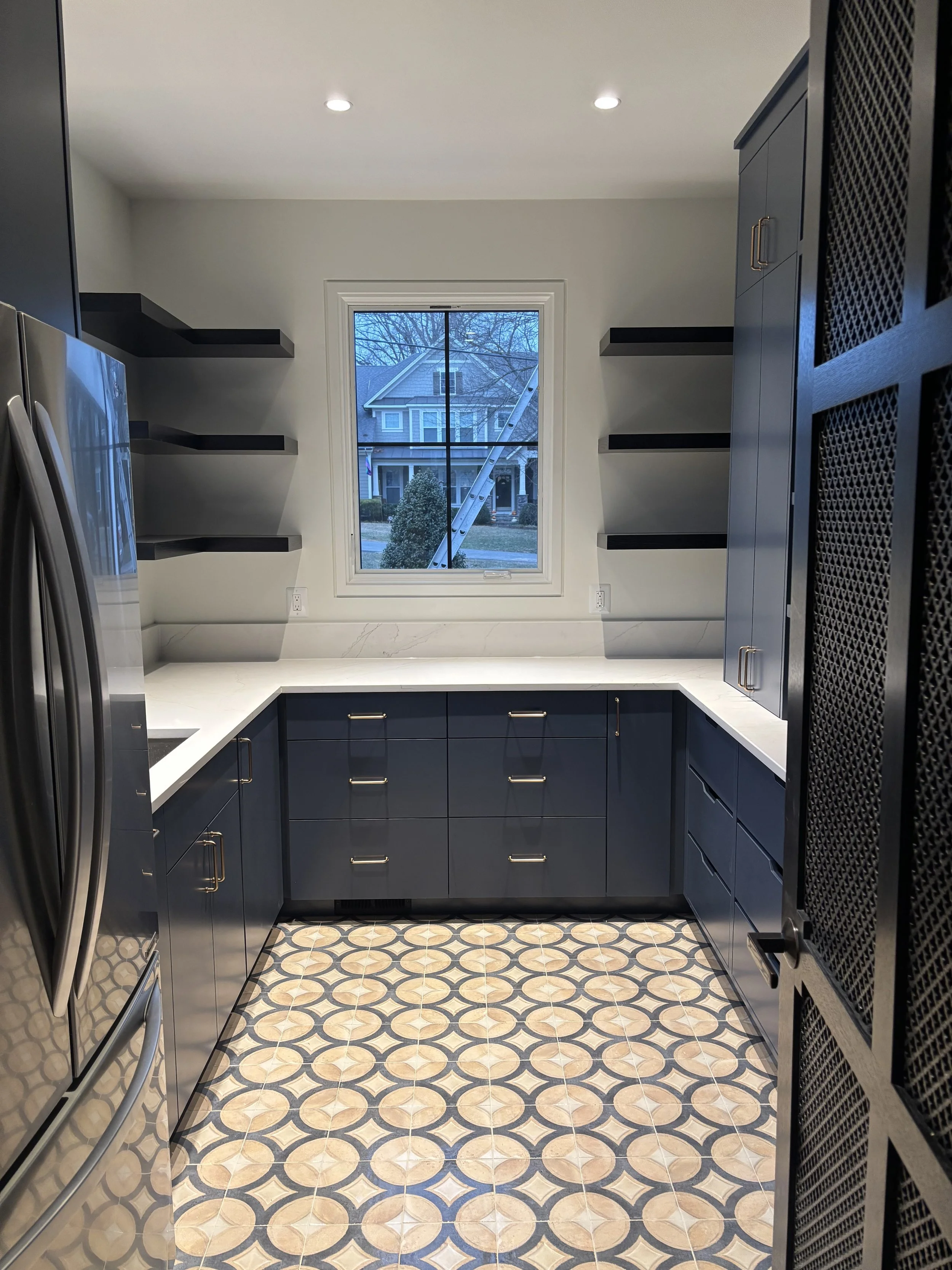 Home scullery featuring blue cabinetry and earthy terracotta-colored floor tiles behind a Jali door.