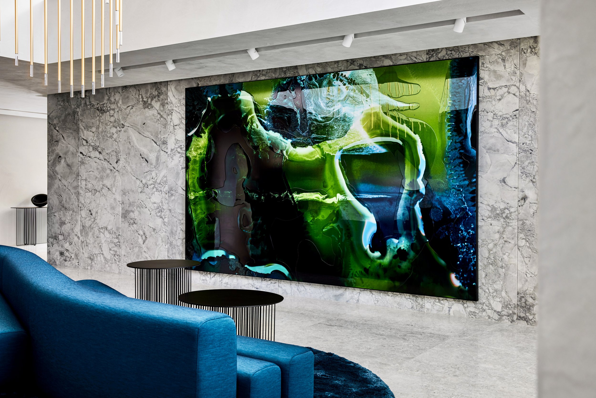 Modern living room with marble wall and a large abstract digital art display featuring vivid green, blue, and black colors.