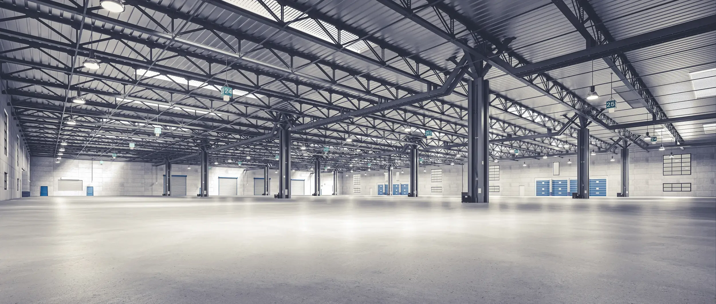 Empty indoor warehouse with high ceiling, metal beams, and overhead lights.